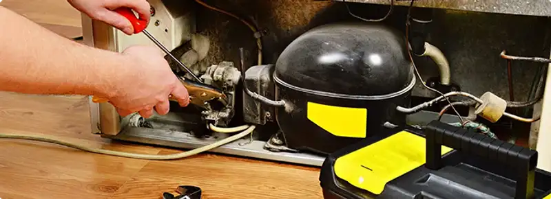 Refrigerator repair technician fixing the compressor and wiring in Peoria, IL